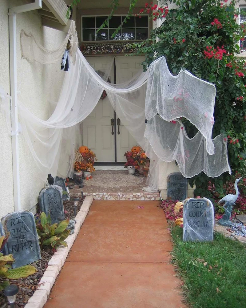 entrée de maison transformée en cimetière d'Halloween avec pierres tombales et gaze blanche