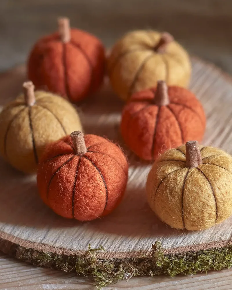 Petites citrouilles décoratives en feutre de laine orange et moutarde sur un rondin de bois