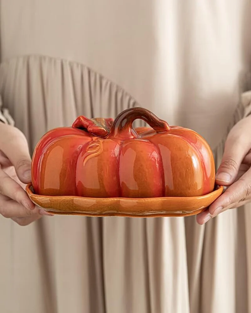 Beurrier en porcelaine orange en forme de citrouille tenu à deux mains