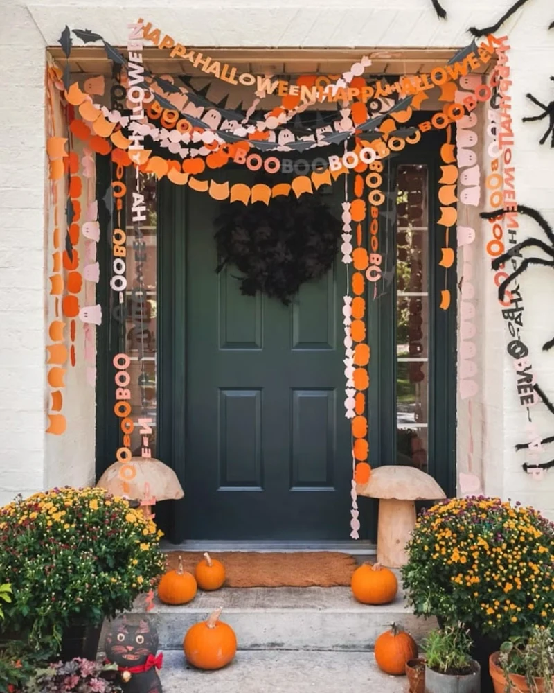 porte d'entrée décorée de guirlandes Halloween en papier orange et rose, chrysanthèmes et citrouilles