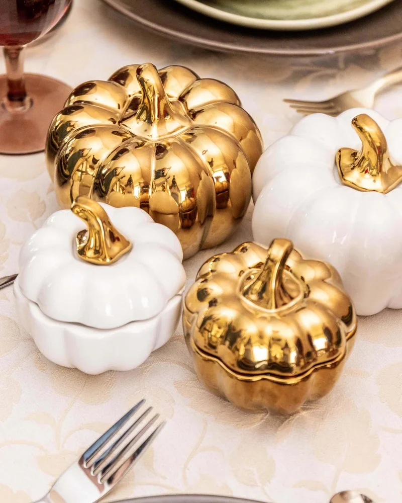 Citrouilles décoratives en porcelaine blanche et dorée posées sur une nappe de fête