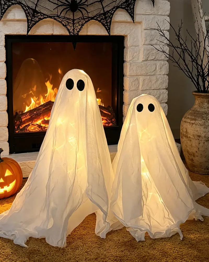 Deux fantômes lumineux en gaze blanche devant une cheminée décorée pour Halloween