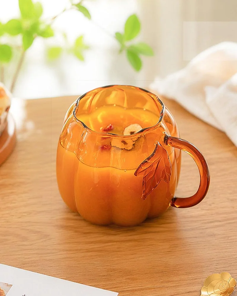 Mug en verre ambré en forme de citrouille avec anse feuille sur une table en bois