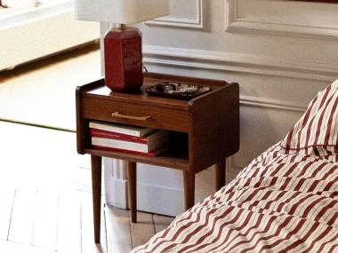 Table de chevet Rodolphe en noyer avec tiroir et niche à côté d'un lit au linge rayé