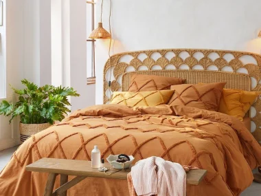 Tête de lit en rotin tressé à motif d'écailles dans une chambre lumineuse au linge orange