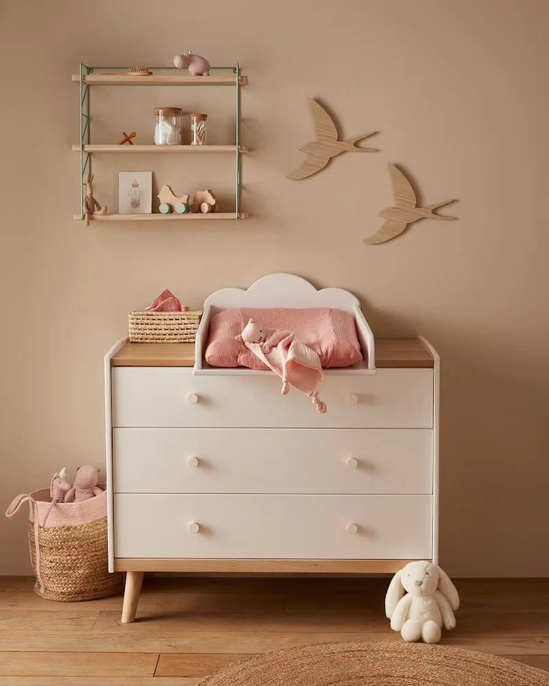 Commode bébé blanche à plateau en bois et pieds compas dans une chambre aux murs rose poudré