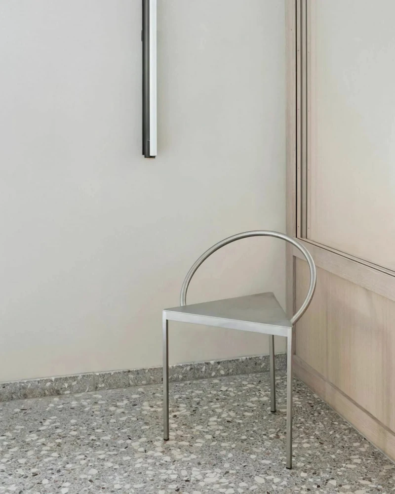Chaise Triangolo de Frama en acier argenté à assise triangulaire et dossier arrondi dans une pièce blanche