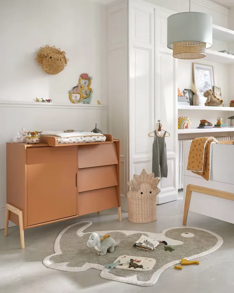 Commode bébé couleur caramel avec porte et tiroirs sur pieds en bois dans une chambre lumineuse