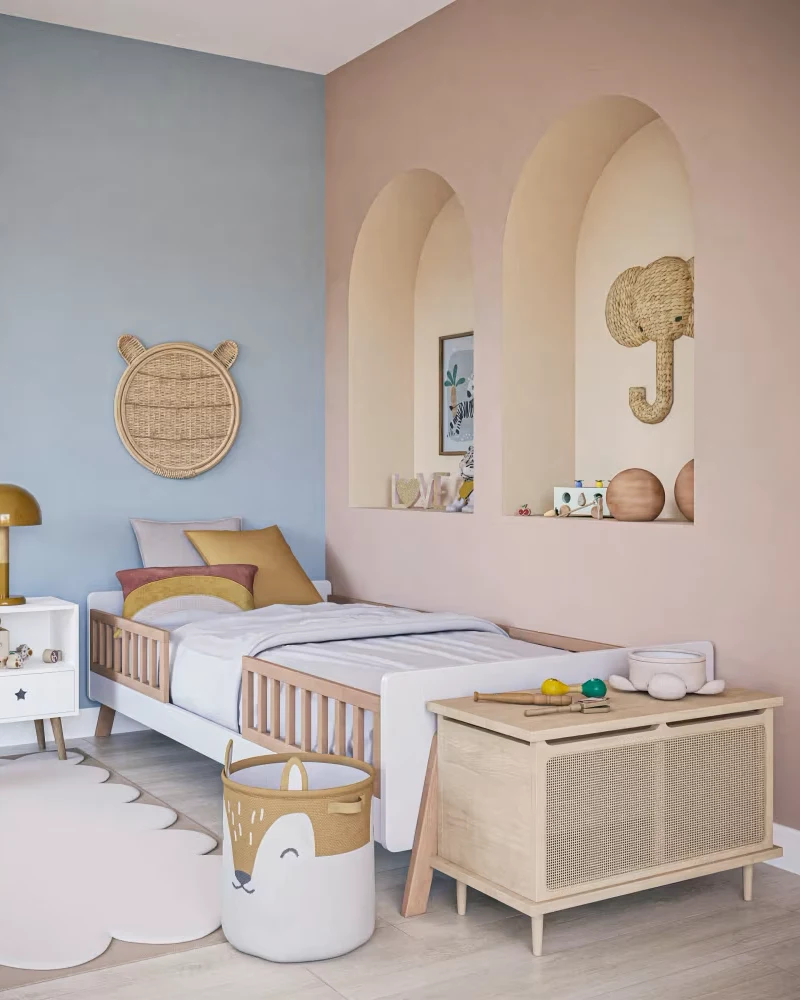 Lit enfant au cadre blanc avec barrière à barreaux en bois clair et pieds en bois dans une chambre bleue et rose