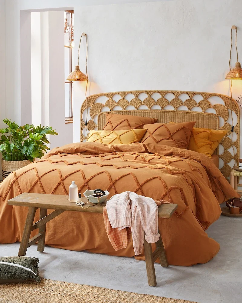 Tête de lit Palma en rotin tressé à motif d'écailles derrière un lit au linge orange