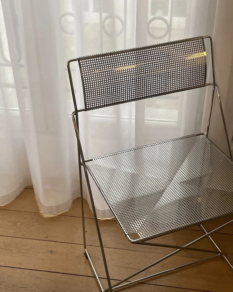 Chaise X-Line de Hay en métal chromé à assise et dossier grillagés devant un voilage blanc