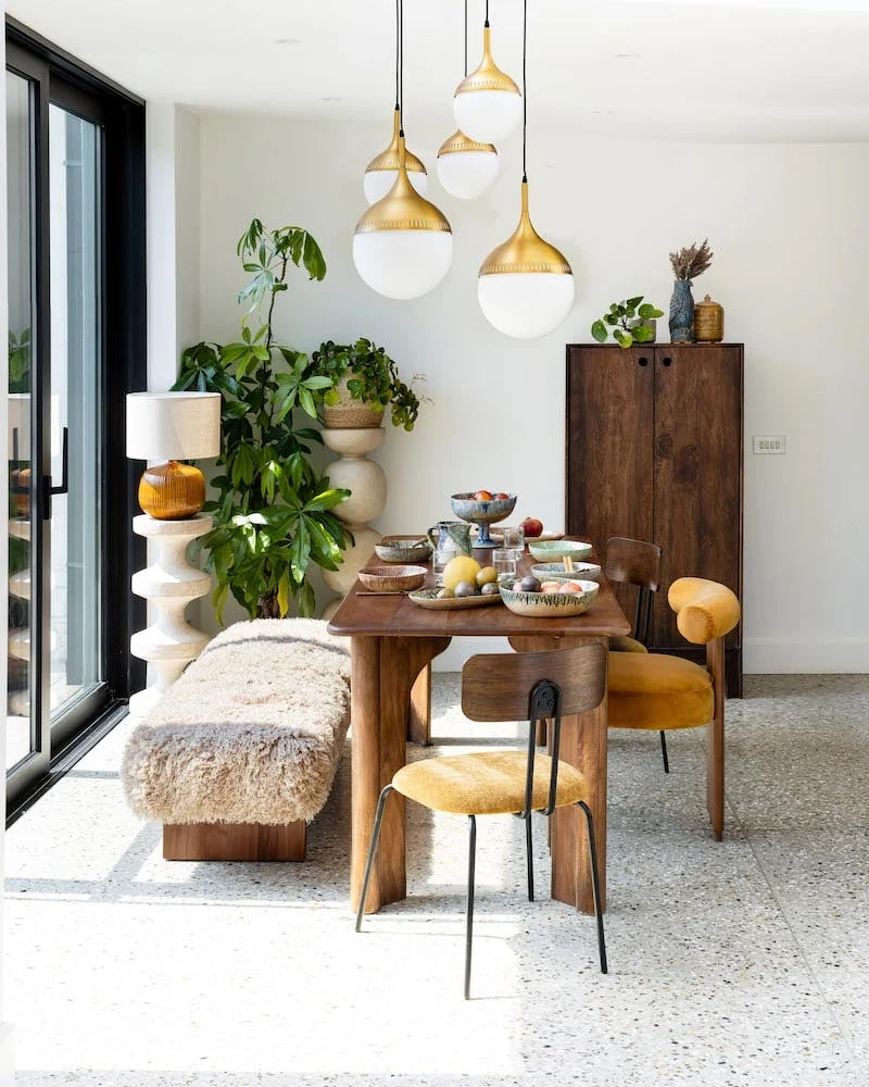salle à manger ethnique moderne avec globes en laiton, table en bois, banc en fourrure et chaise moutarde