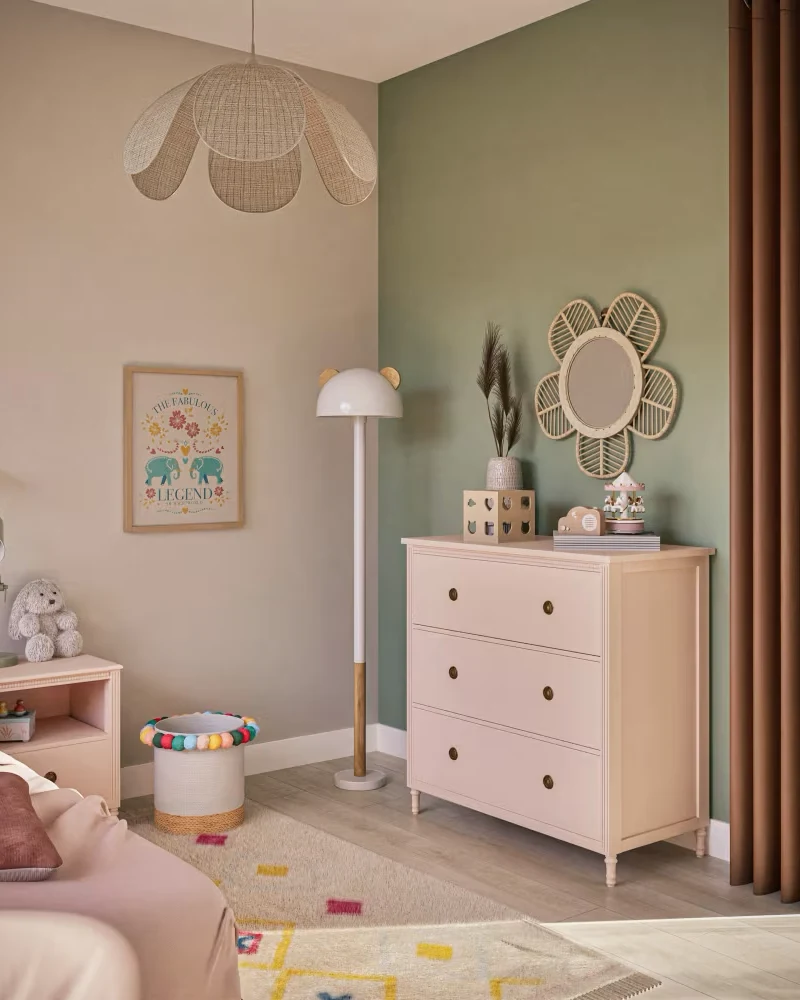 Commode bébé rose pâle à trois tiroirs dans une chambre aux murs vert sauge et rose