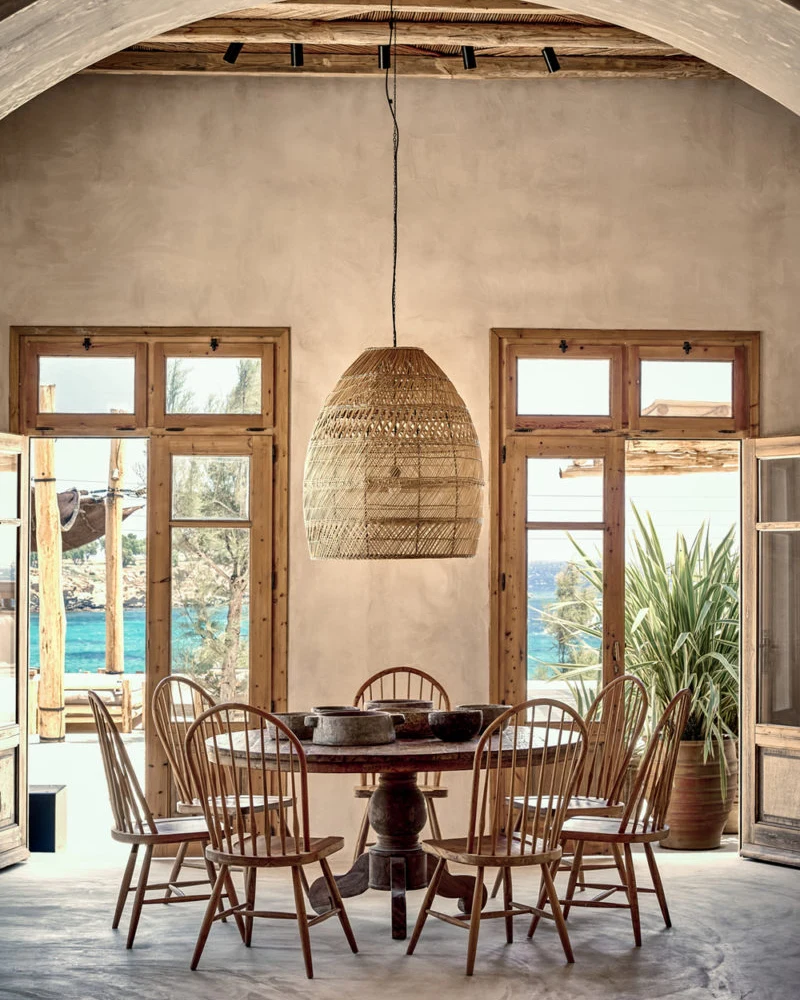 salle à manger ethnique minimaliste avec mur arrondi en enduit, table ronde, chaises en bois et suspension en osier