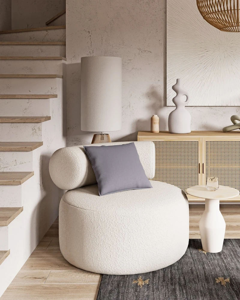 Fauteuil pivotant rond en bouclette gris très clair avec coussin dans un salon beige près d'un escalier