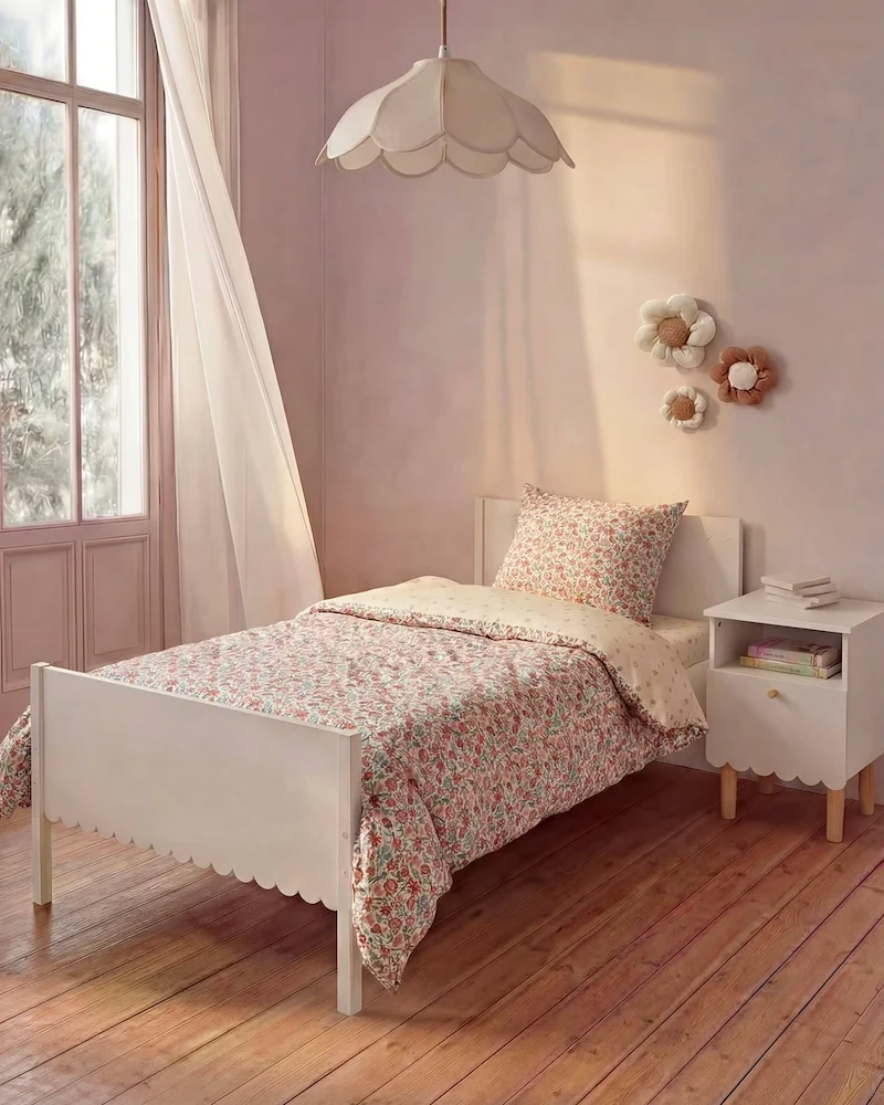 Lit enfant blanc à tête et pied de lit festonnés dans une chambre rose avec linge fleuri
