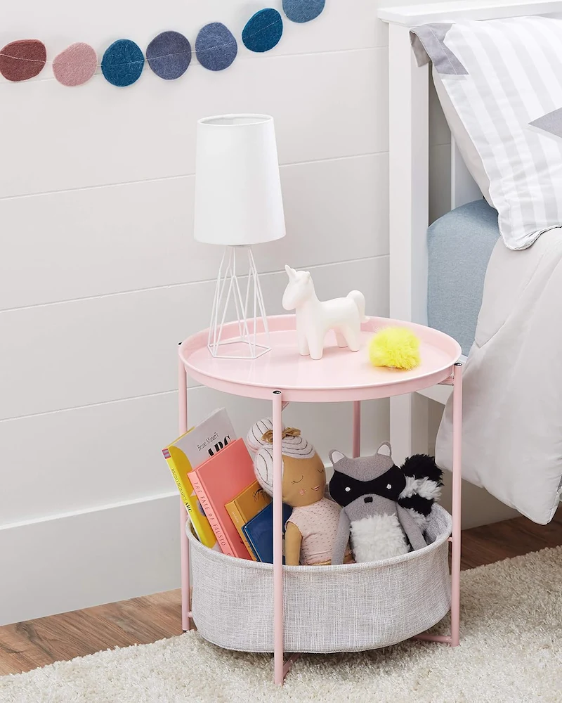 Table d'appoint ronde rose avec plateau et panier de rangement en tissu à côté d'un lit enfant