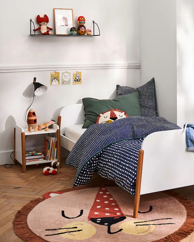 Petite table de chevet enfant ouverte blanc et bois clair remplie de livres près d'un lit blanc