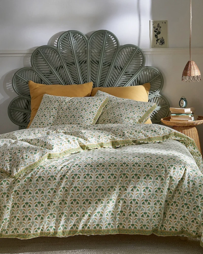 Tête de lit Paoni en rotin en forme de fleur ou d'éventail derrière un lit au linge imprimé