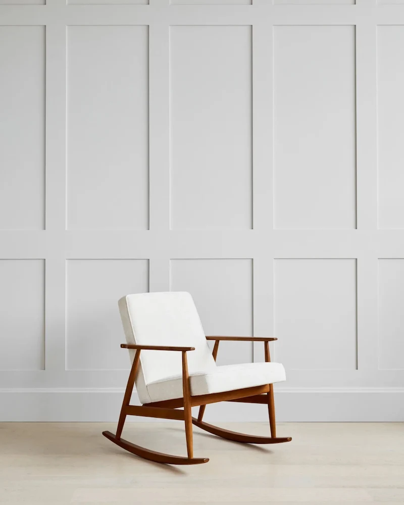 Fauteuil à bascule Fox de 366 Concept en velours côtelé crème et frêne foncé devant un mur à moulures