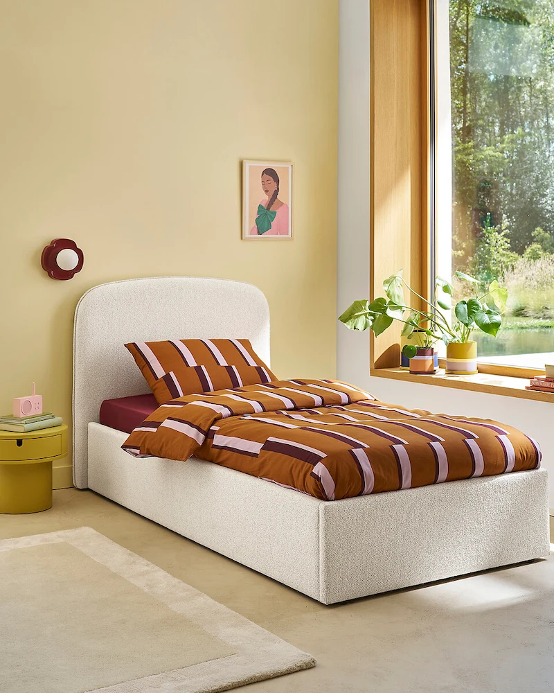Lit enfant tapissé d'un tissu écru à l'aspect texturé avec tête de lit arrondie dans une chambre jaune pâle