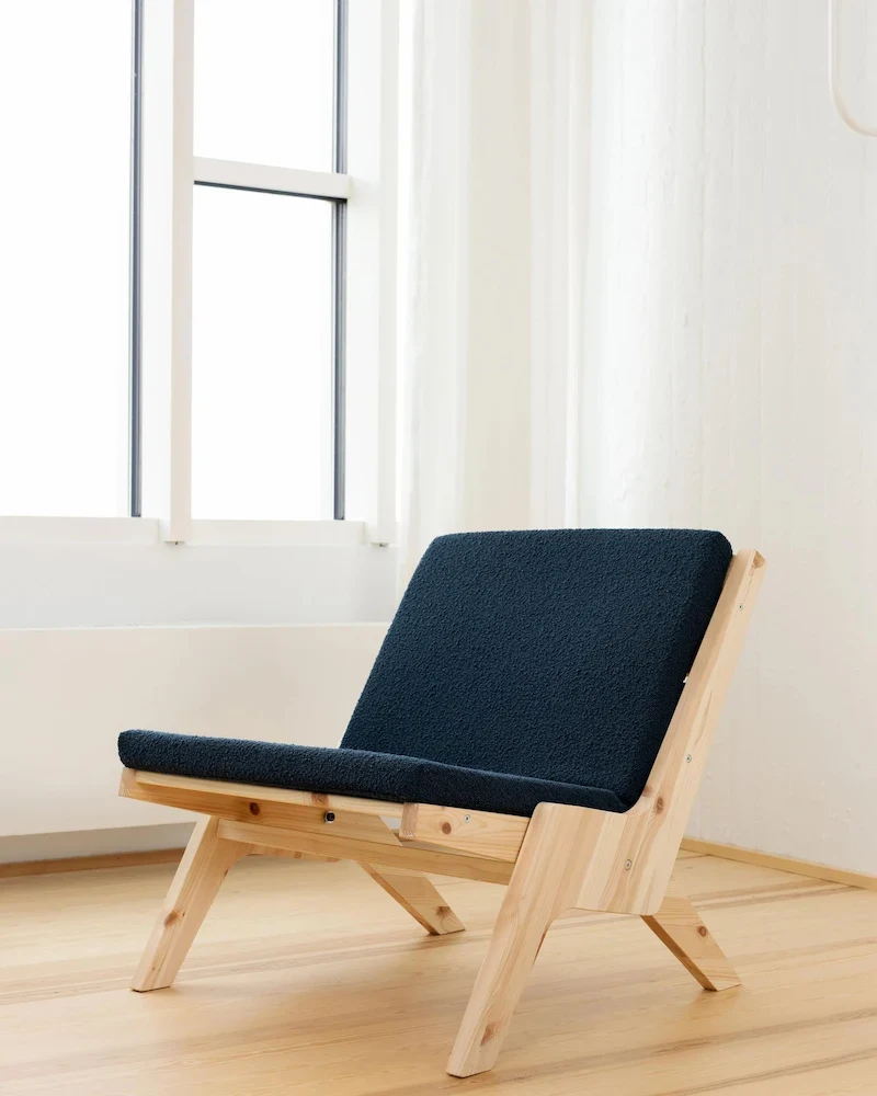 Fauteuil lounge Sway de Karup Design en pin massif et coussin bleu dans un salon lumineux
