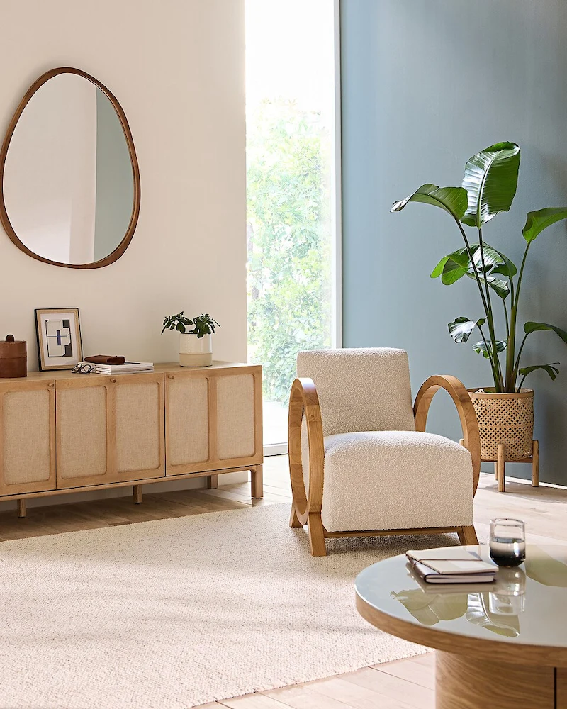 Fauteuil vintage Berti en bouclette écrue avec accoudoirs arrondis en chêne massif dans un salon lumineux