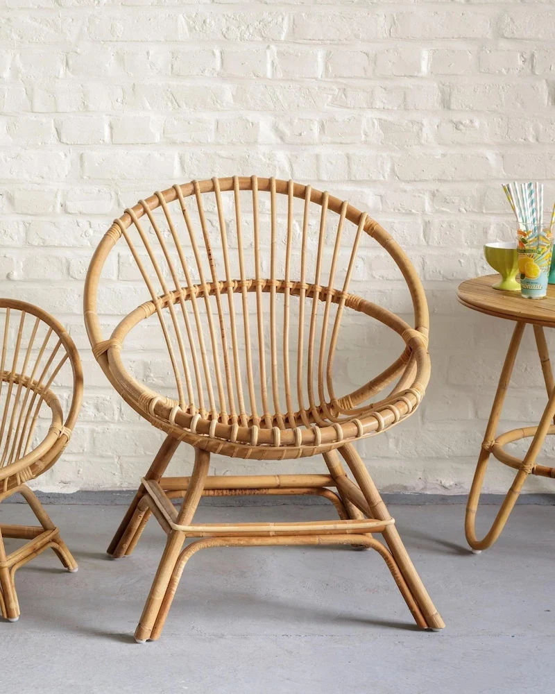 Fauteuil coquille Brigitte de KOK en rotin naturel devant un mur de briques blanches