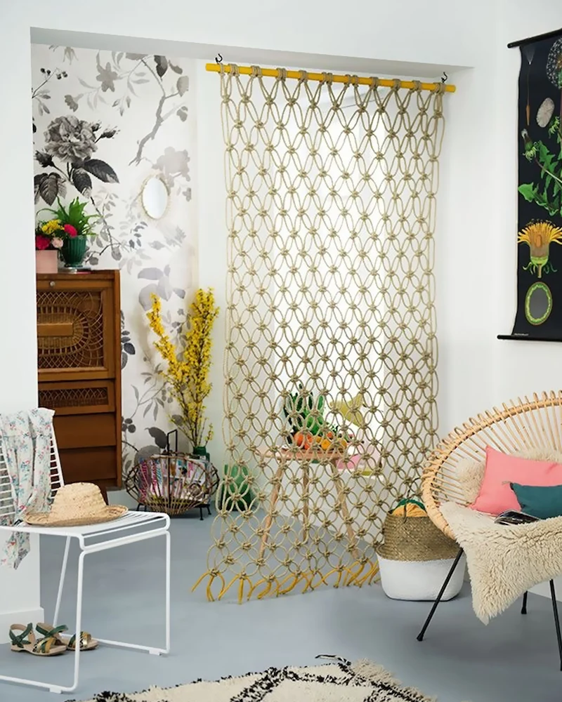 Cloison suspendue en macramé de corde naturelle devant un mur à motifs