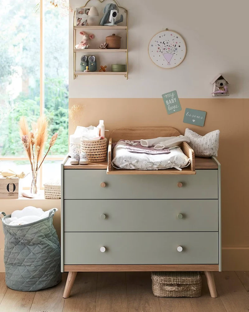 Commode bébé vert grisé avec plateau en bois et plan à langer posé dessus dans une chambre claire