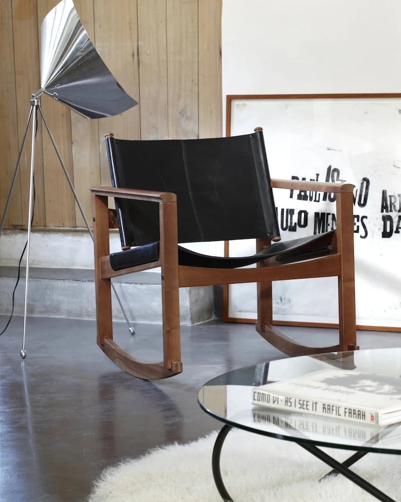 Fauteuil à bascule Peglev d'Objekto en cuir noir et noyer dans un salon avec table basse en verre