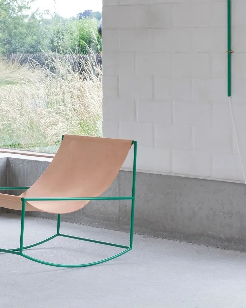 Fauteuil à bascule de Muller Van Severen en métal vert et cuir tendu naturel dans une pièce en béton