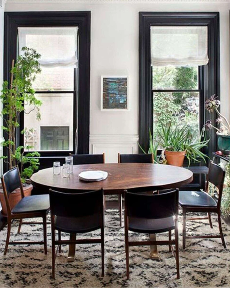 salle à manger ethnique noire avec fenêtres noires, table ronde en bois, chaises sombres et tapis berbère