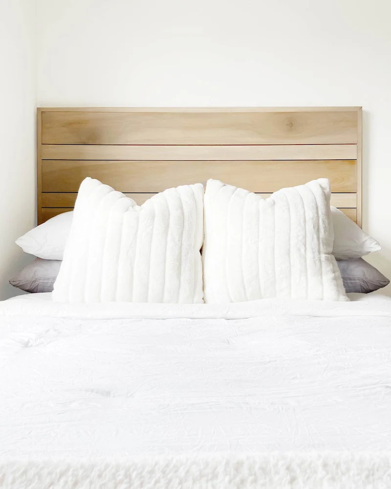 Tête de lit en planches de bois clair horizontales encadrées derrière un lit au linge blanc