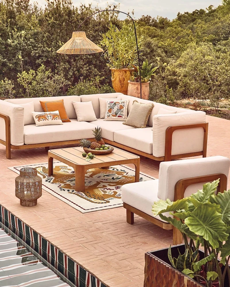 Ensemble canapé d'angle de jardin en eucalyptus et coussins écrus avec table basse sur une terrasse en terre cuite