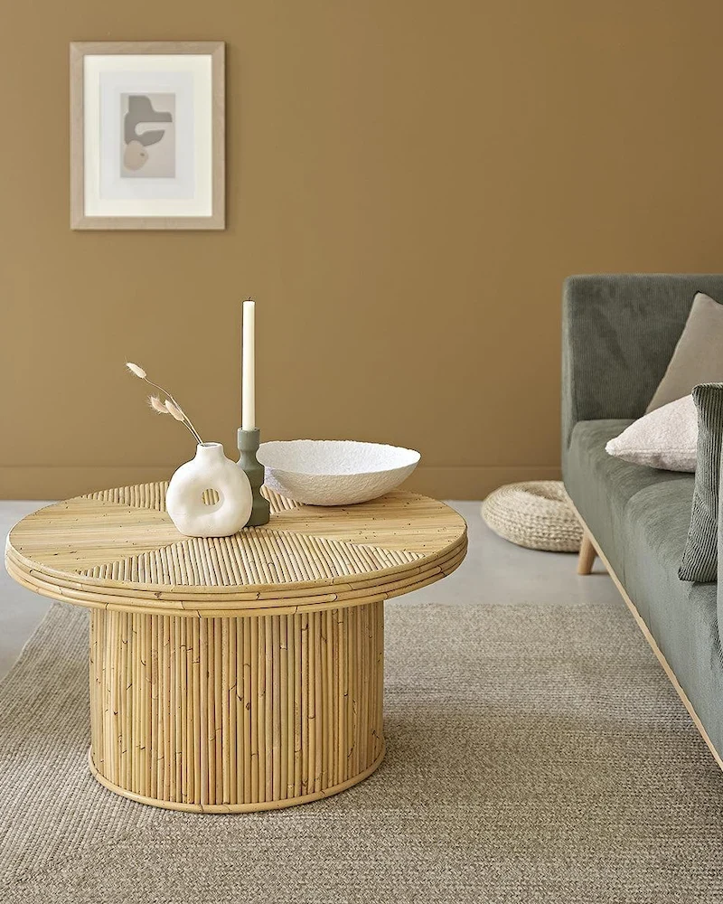 Table basse ronde Alma en canne de rotin coloré naturellement devant un canapé vert