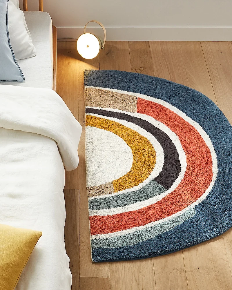 Tapis arc-en-ciel Niji en coton bio AM.PM au pied d'un lit