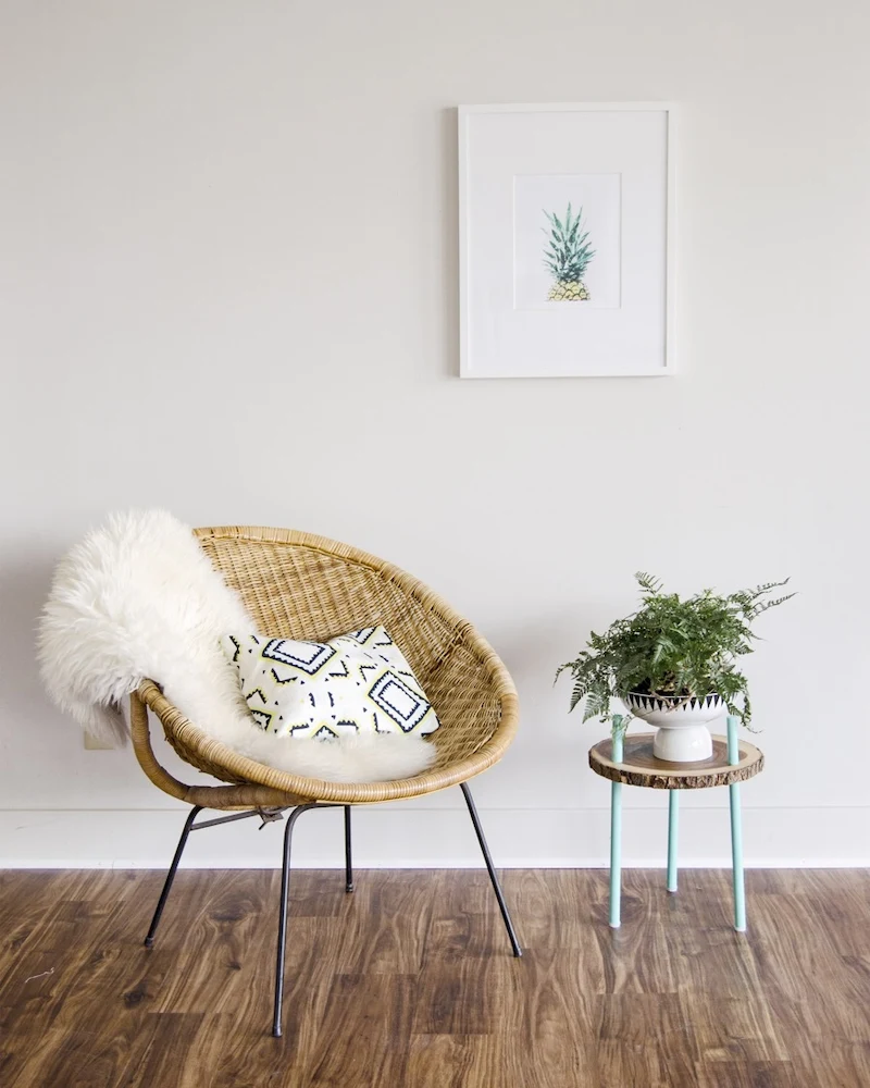 Support de plante en rondin de bois sur trois pieds en tourillons à côté d'un fauteuil