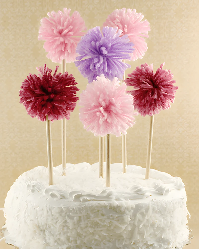 Gâteau blanc surmonté de pompons en laine sur des pics