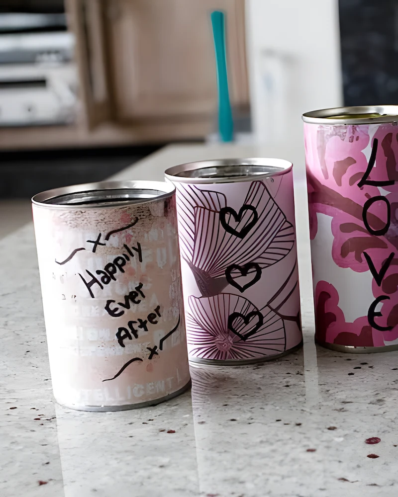 Boîtes de conserve recouvertes de papiers roses et bleus à cœurs, avec les mots Just Married