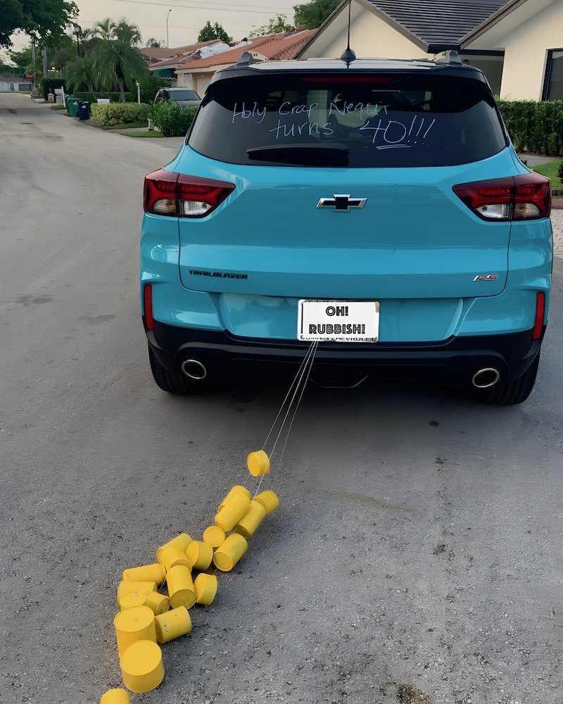 Voiture bleue avec une traîne de boîtes de conserve peintes en jaune attachées au pare-chocs