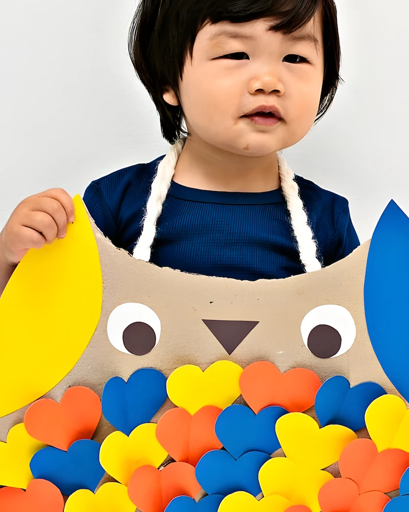 Enfant portant un costume de hibou en carton avec des plumes en cœurs colorés
