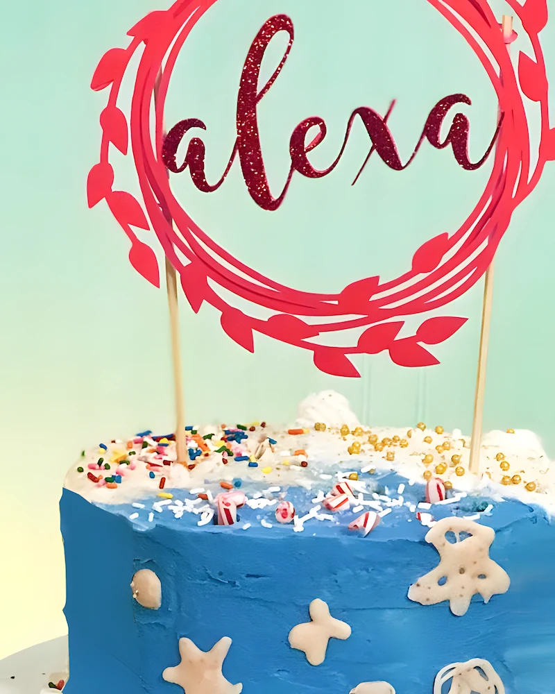 Gâteau bleu surmonté d'un topper rose avec le prénom Alexa dans une couronne