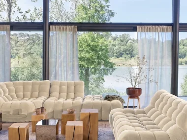 Grand salon lumineux avec angle modulable capitonné Jud en velours écru face à une baie vitrée
