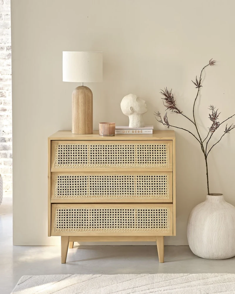 Commode en bois et cannage avec lampe et vase blanc, dans une pièce claire