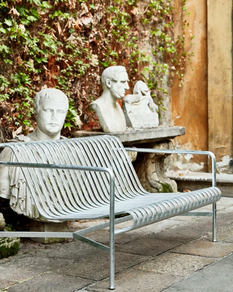 Banc de jardin Palissade de HAY en métal gris dans une cour pavée avec des statues